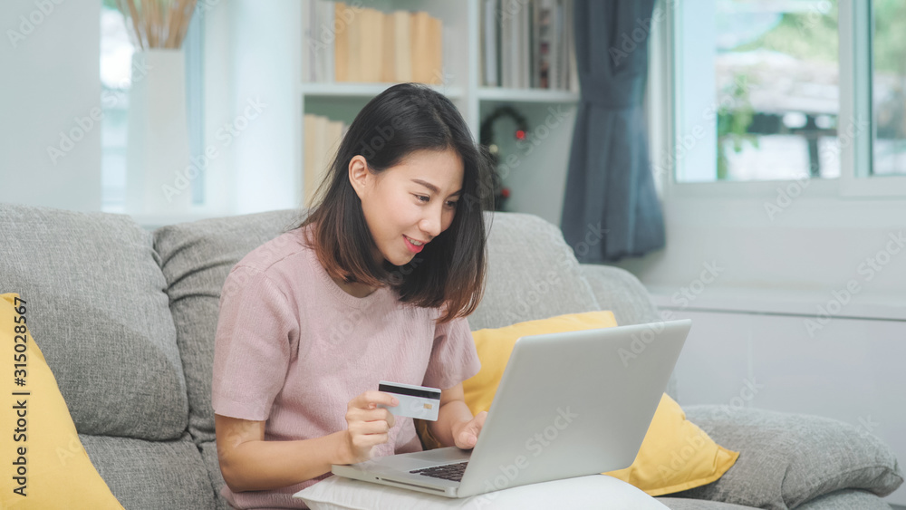 Asian woman using laptop and credit card shopping ecommerce, female relax feeling happy online shopping sitting on sofa in living room at home. Lifestyle women relax at home concept. Asian woman using laptop and credit card shopping ecommerce, female relax feeling happy online shopping sitting on sofa in living room at home. Lifestyle women relax at home concept.