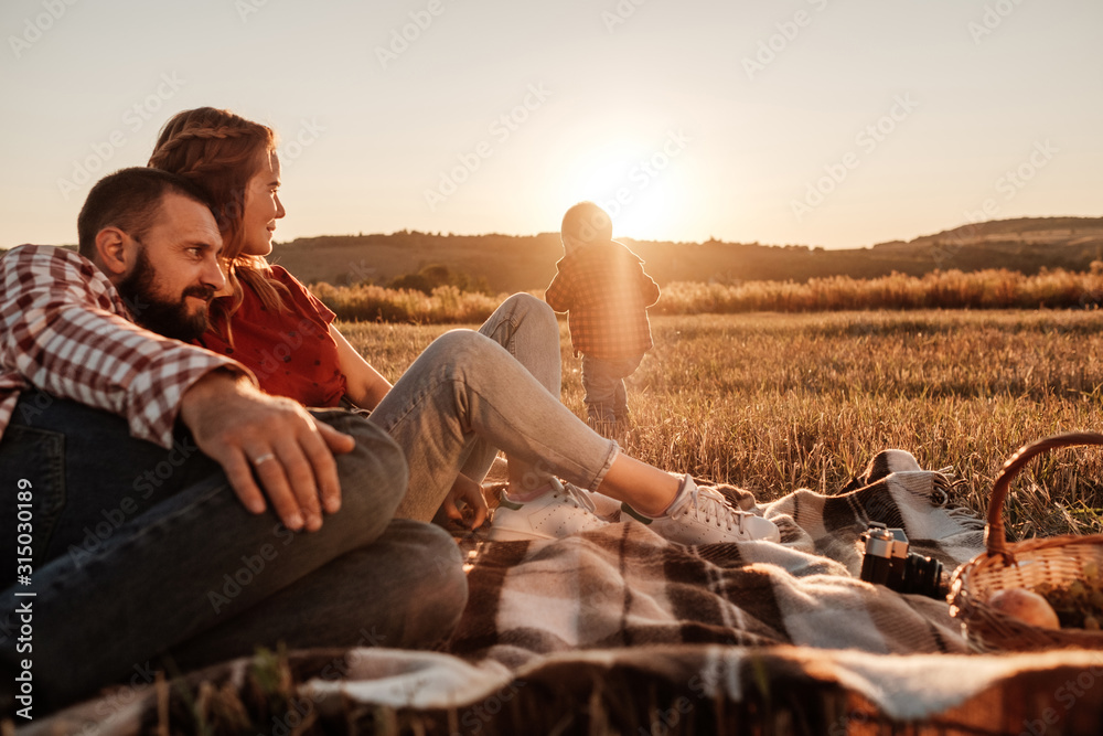 Happy Young Family Mom and Dad with Their Little Son Enjoying Summer Weekend Picnic Outside the City in the Field at Sunny Day Sunset, Vacation Time Concept