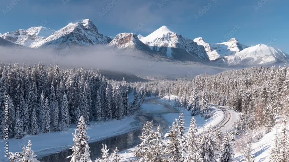 Snowy mountain time-lapse of Morant's curve in Banff National Park which features mountains, forests, a river, and railroad track in a winter wonderland.