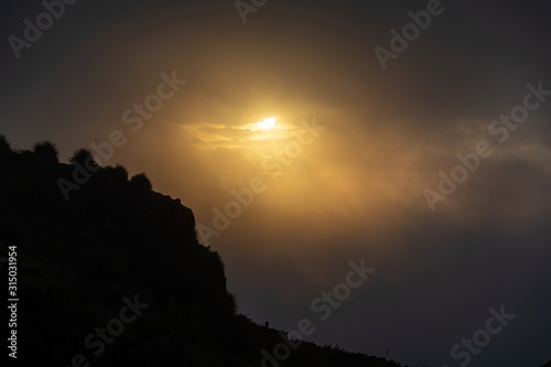 View of coastal cliff silhouette back-lit with evening sun dimmed by thick fog