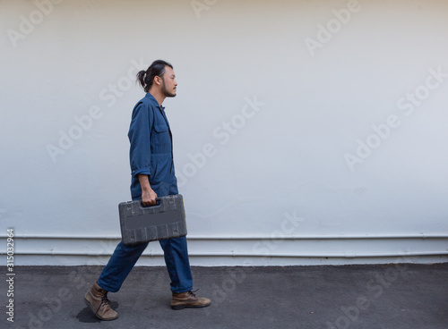 Asian mechanic in blue uniform holding tool box walking to workplace