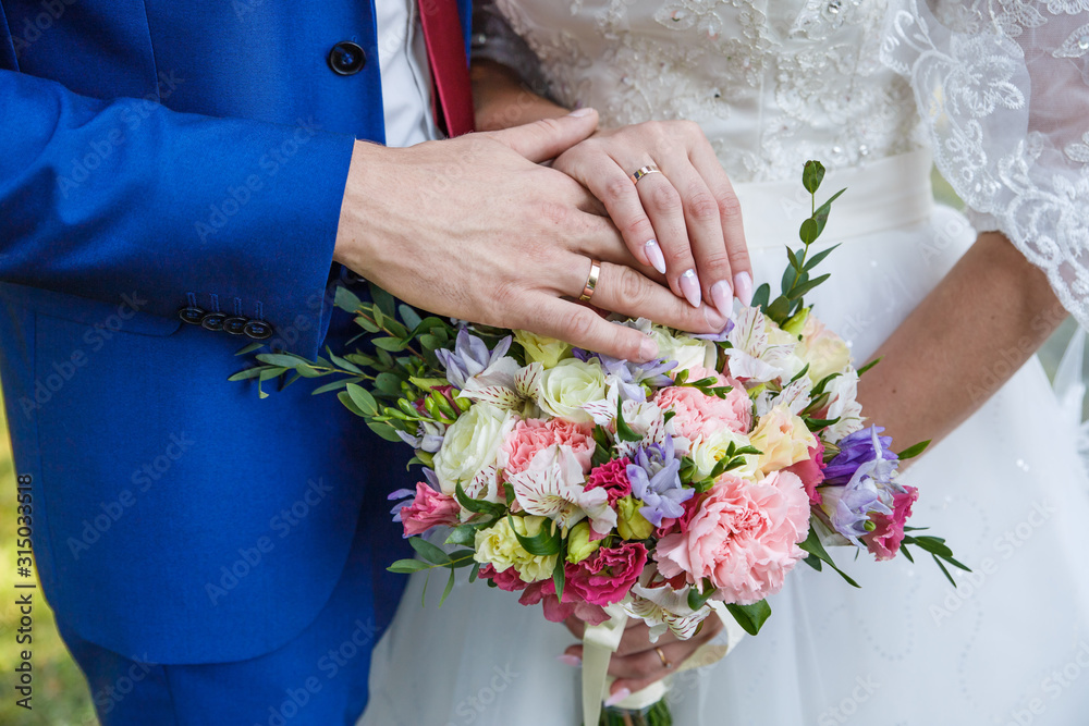 Hands of newlyweds with wedding rings and a bouquet of flowers. The groom in a blue suit and red tie. The concept of wedding love and Valentine's day Hands of newlyweds with wedding rings and a bouquet of flowers. The groom in a blue suit and red tie. The concept of wedding love and Valentine's day