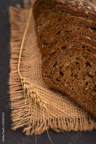 Pieces of sliced ​​bread lie on jute napkin. Nearby lie one spikelet of wheat