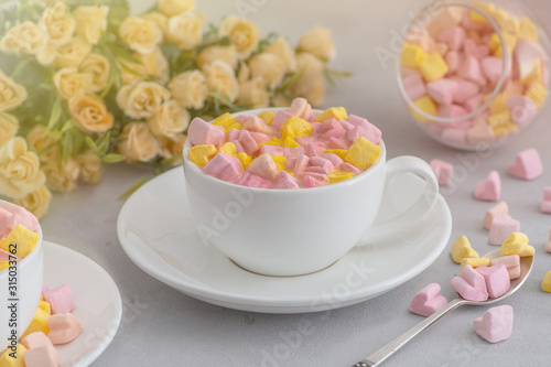Cup of coffee with marshmallows stands on a table with flowers lit by sunlight