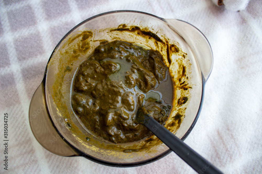 Fototapeta premium Mixing henna with a wooden spoon in a bowl for hair application of natural color like Indian henna mix.