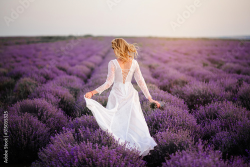 Young woman in white dress walks through blooming lavender field at sunset