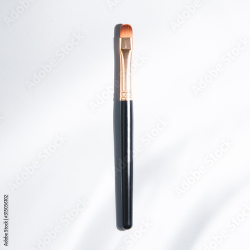Light background with highlights for the site. A tool for a makeup artist. Makeup brush. Black plastic eyebrow brush.