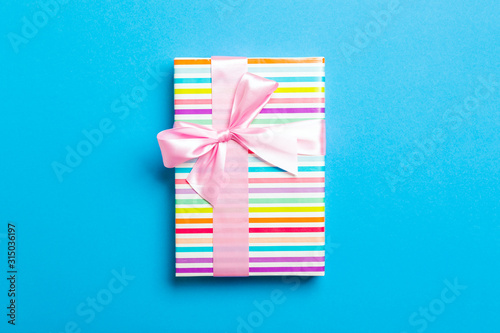 wrapped Christmas or other holiday handmade present in paper with pink ribbon on blue background. Present box, decoration of gift on colored table, top view with copy space
