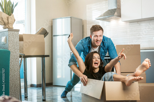 young couple husband and wife having fun while unpacking boxes and moving in new appartment. husband carrying his wife in box on the floor
