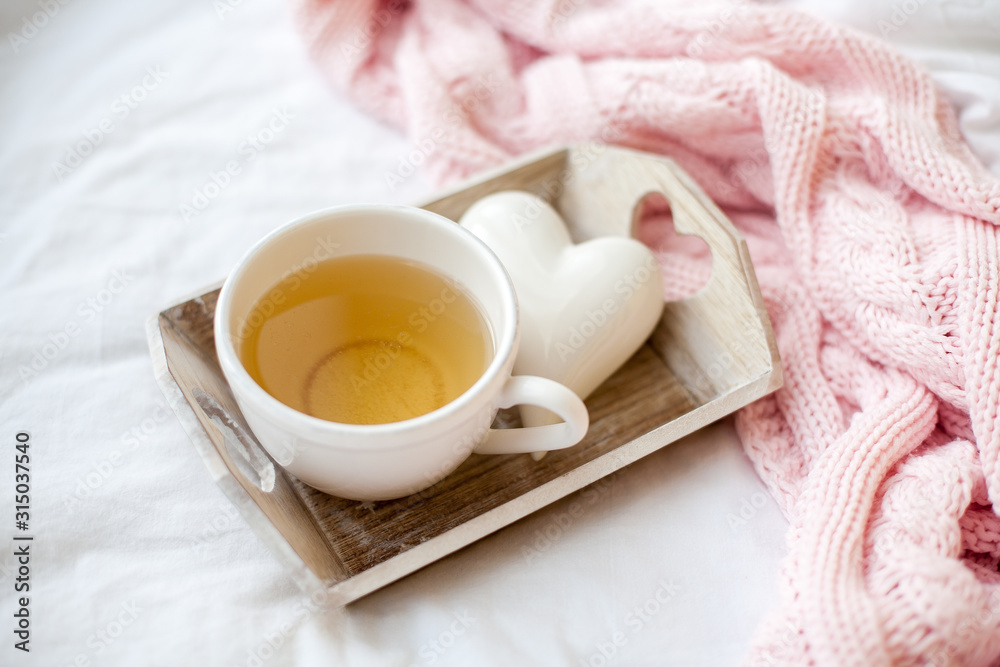 Beautiful white cup with tea on the bed, pink knitted plaid, decor Valentine's Day. Breakfast in bed. Morning. Spring. Cozy. Beautiful white cup with tea on the bed, pink knitted plaid, decor Valentine's Day. Breakfast in bed. Morning. Spring. Cozy.