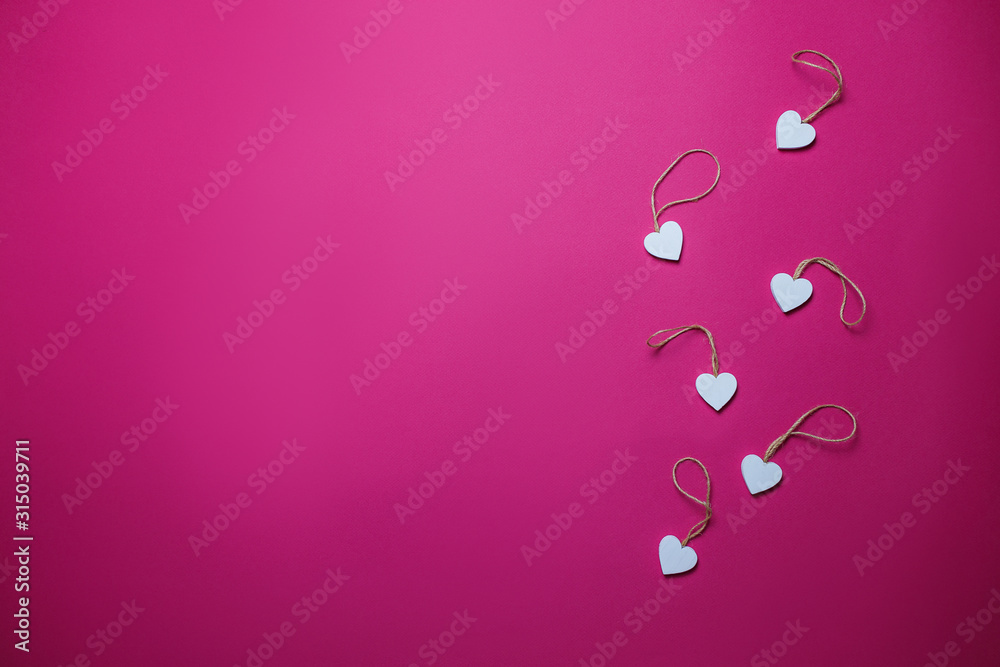 Small white wooden hearts on pink background with copy space. Saint Valentine's day card on pink background.