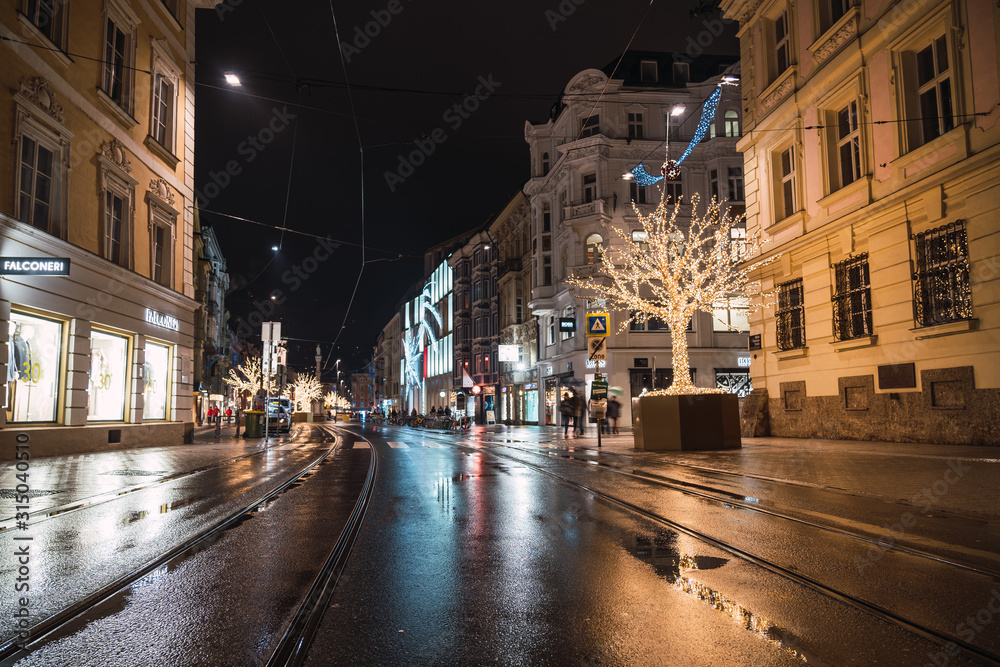 Shopping and pedestrian street with the rails of the tram lit up at night and a Christmas tree