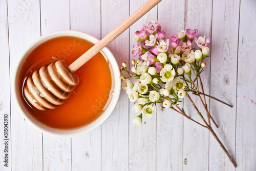 Pink and white manuka flower and honey in a white bowl and dipper in it