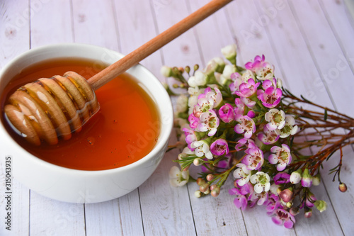 Pink and white manuka flower and honey in a white bowl and dipper in it
