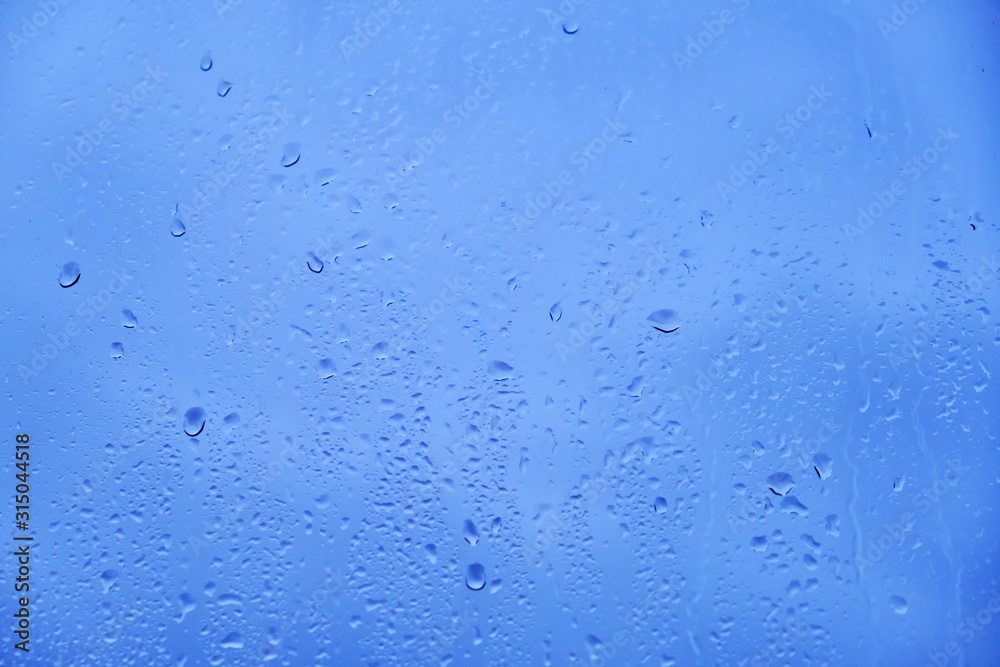 Glass background with big drops of rain. Autumn window with the texture of water drops against a cloudy blue sky Glass background with big drops of rain. Autumn window with the texture of water drops against a cloudy blue sky