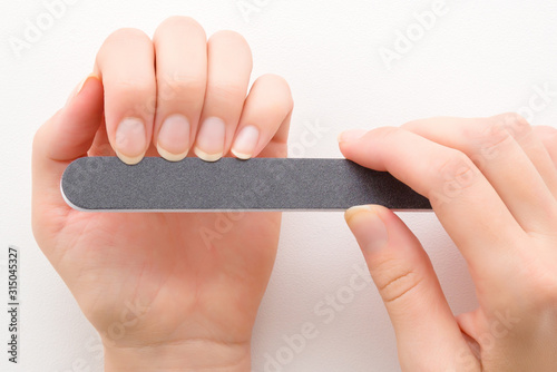 Canvas Print Woman hands using black nail file on white table background