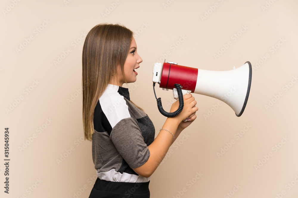 Teenager girl over isolated background shouting through a megaphone Teenager girl over isolated background shouting through a megaphone