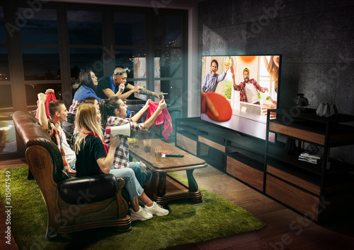 Group of friends watching TV, table tennis match, leisure activity. Emotional men and women cheering for favourite team, look on fighting for ball. Concept of friendship, sport, competition, emotions.