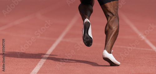 African-american male sportsman running on stadium track, dynamic run of sprinter in a stadium