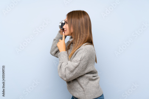 Teenager girl with sweater over isolated blue background holding a camera © luismolinero