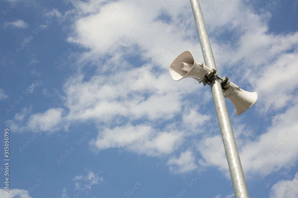 Loudspeaker of siren / alarm. Audio device for making loud noise and producing warning sound that warns and alerts public during danger and emergency. Sunny blue sky with clouds as copy space Loudspeaker of siren / alarm. Audio device for making loud noise and producing warning sound that warns and alerts public during danger and emergency. Sunny blue sky with clouds as copy space