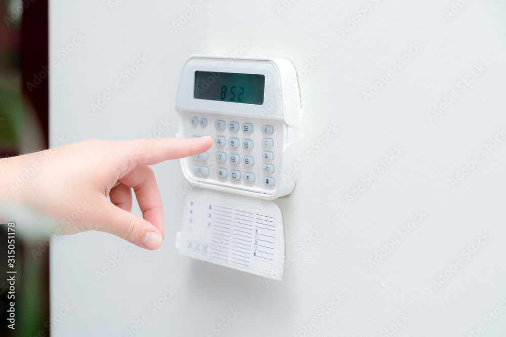 Woman hand entering alarm system password of an apartment, house of business office. Surveillance and protection console against rubbery and thief Woman hand entering alarm system password of an apartment, house of business office. Surveillance and protection console against rubbery and thief