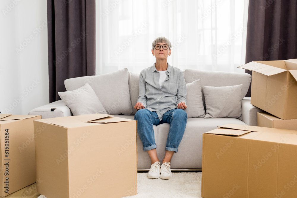 mature woman sitting on sofa and meditating in new house mature woman sitting on sofa and meditating in new house