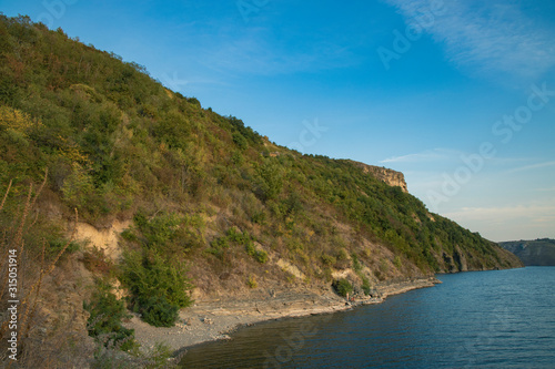summer time nature reservation landscape of green hill coast of lake water shoreline with blue sky background