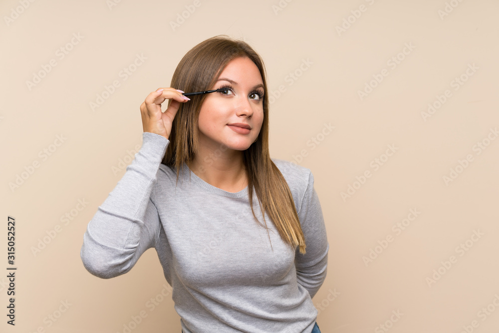 Teenager girl applying mascara with cosmetic rush over isolated background Teenager girl applying mascara with cosmetic rush over isolated background