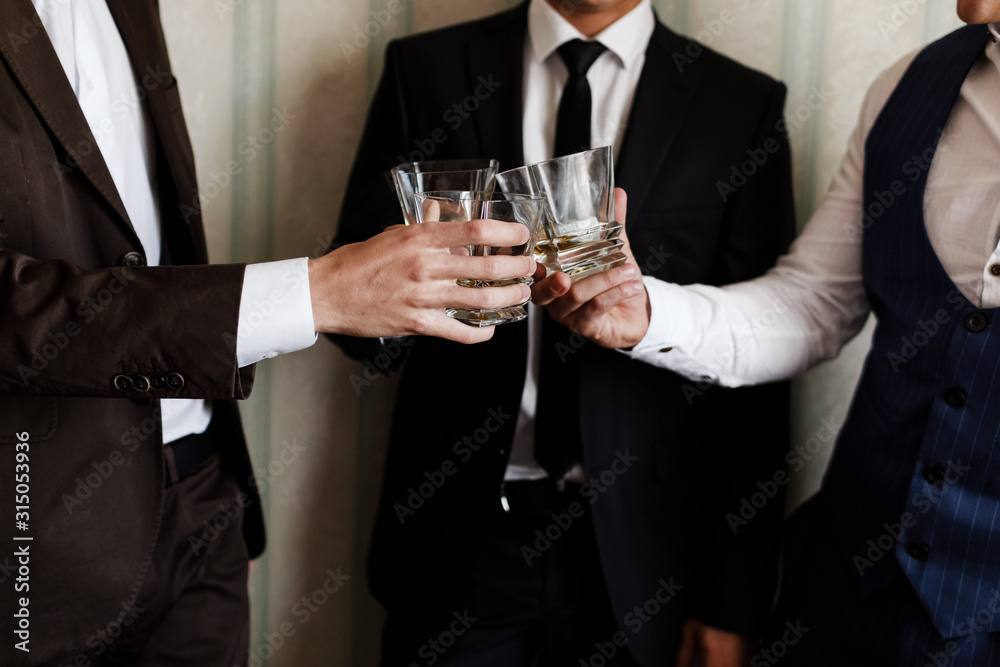 stylish friends businessmen in suits toasting with glasses of whiskey indoors, closeup. groom's morning