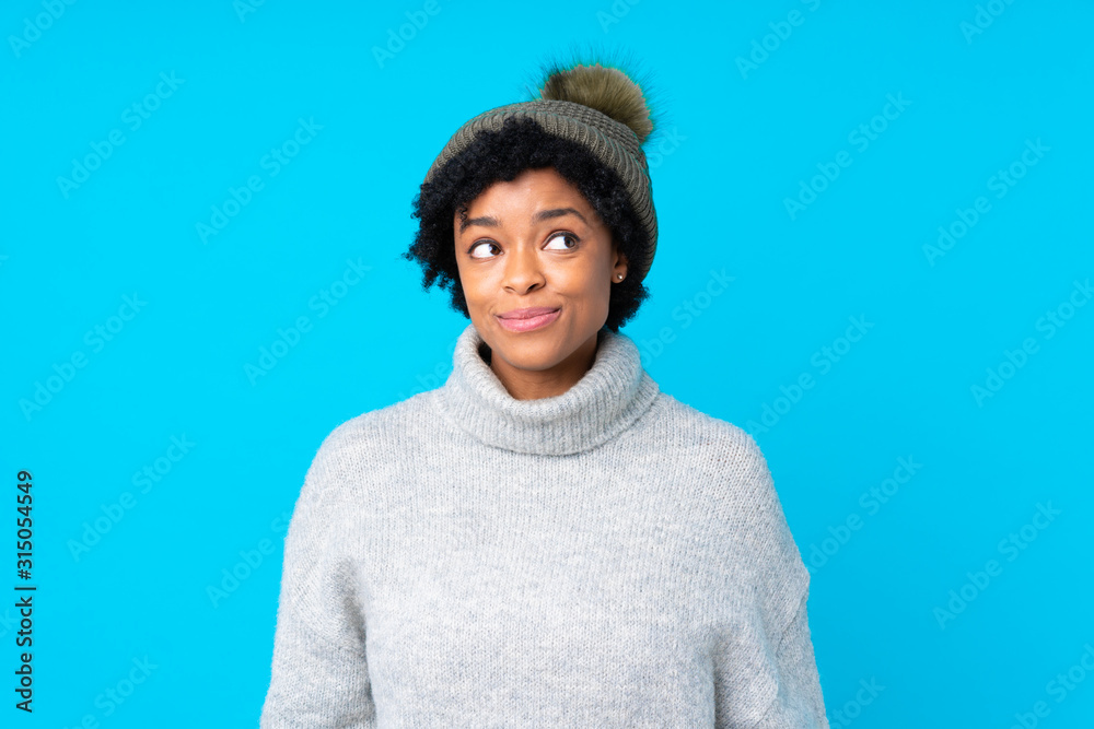 African american woman with winter hat over isolated blue background laughing and looking up African american woman with winter hat over isolated blue background laughing and looking up