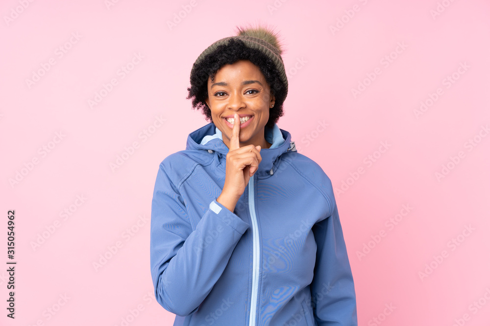 African american woman with winter hat over isolated pink background doing silence gesture