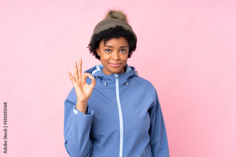 African american woman with winter hat over isolated pink background showing an ok sign with fingers African american woman with winter hat over isolated pink background showing an ok sign with fingers