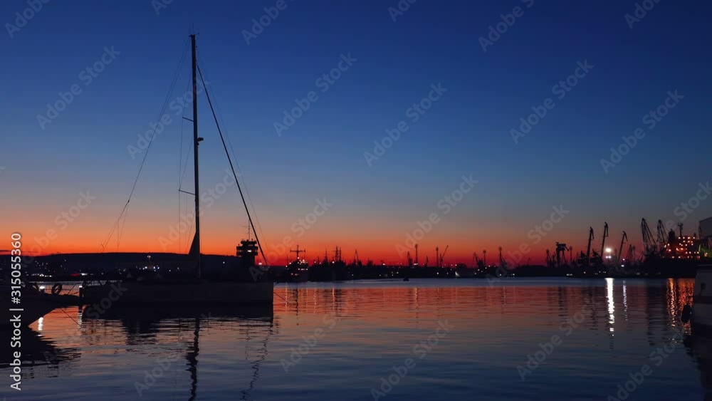 Sunset over the sea port. Yacht, lighthouse and view toward city lights Sunset over the sea port. Yacht, lighthouse and view toward city lights
