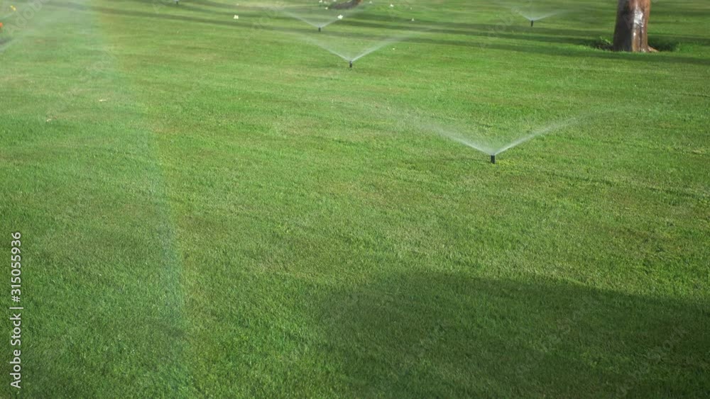 Irrigation system working at green lawns outdoors. Beautiful rainbow seen in falling water drops isolated on green grass background. Real time 4k video footage. Irrigation system working at green lawns outdoors. Beautiful rainbow seen in falling water drops isolated on green grass background. Real time 4k video footage.