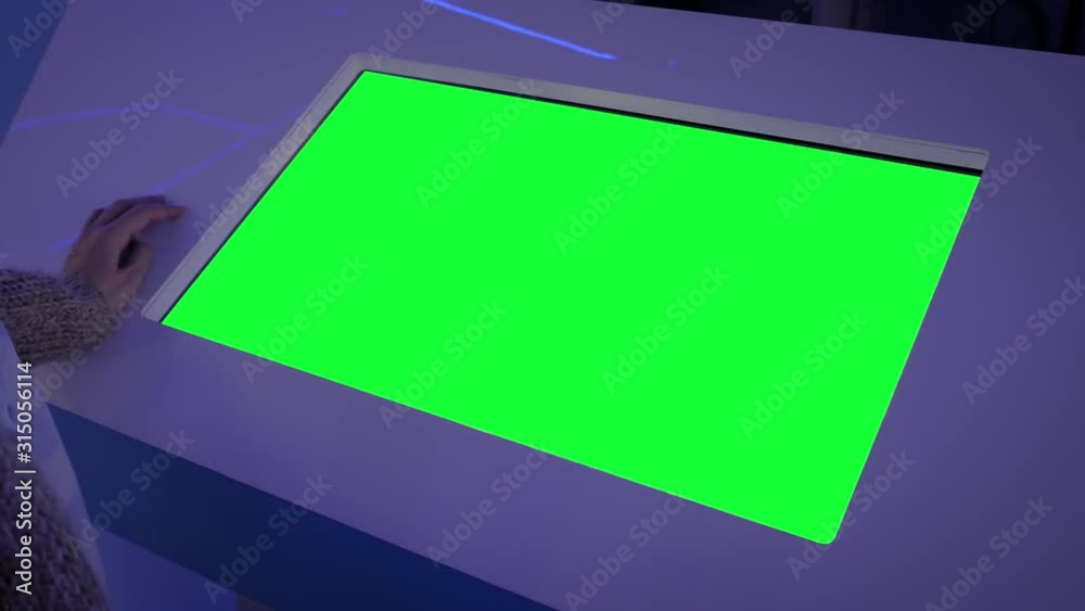 Woman looking at blank digital interactive green display kiosk at exhibition or museum with futuristic sci-fi interior. Mock up, copyspace, template, chroma key, green screen, technology concept
