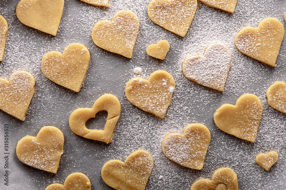 uncooked heart shaped cookies on parchment white paper sprinkled with powdered sugar