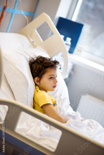 7 years old ill child in yellow t-shirt lying in bed in hospital room after serious nasal surgery. Medical care for children. Healthcare in clinic after surgery. Girl in hospital bed
