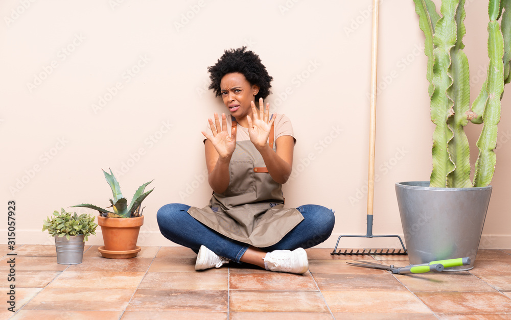 Gardener woman sitting on the floor nervous stretching hands to the front Gardener woman sitting on the floor nervous stretching hands to the front