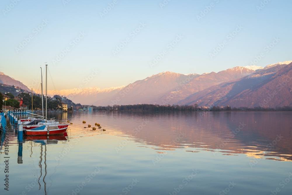 Colorful red boats on stunning mountain lake in Alps during sunset,panorama of Iseo lake from the city of Lovere,Bergamo,Lombardy Italy. Colorful red boats on stunning mountain lake in Alps during sunset,panorama of Iseo lake from the city of Lovere,Bergamo,Lombardy Italy.