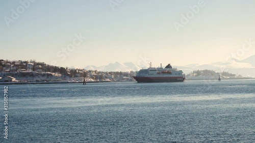 FINNSNES, TROMS, NORWAY, MARCH 11 2019:  cruise service vessel Hurtigruten going along winter fjord shore at sunny day photo