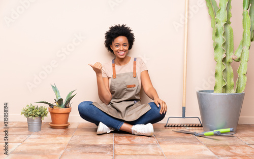 Gardener woman sitting on the floor pointing to the side to present a product