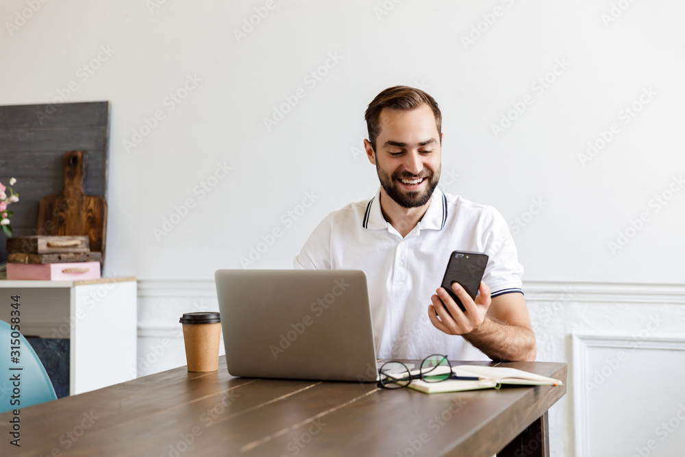 Handsome young bearded man sitting at the table at home Handsome young bearded man sitting at the table at home