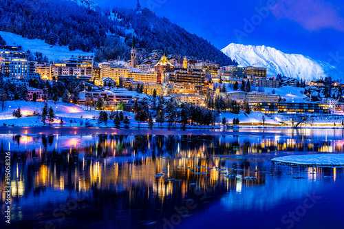 View of beautiful night lights of St. Moritz town in Switzerland at night in winter, with reflection from the lake and snow mountains in backgrouind photo