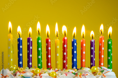 multi-colored candles burn on a birthday cake on a yellow background