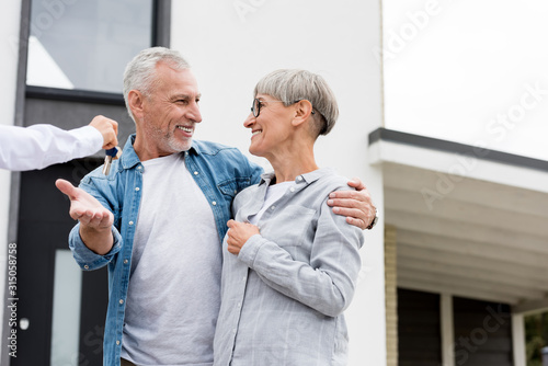 cropped view of broker giving keys of new house to smiling mature man and woman