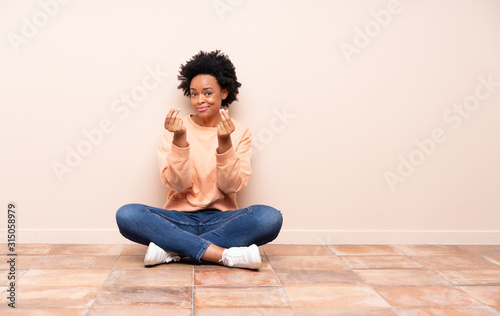 African american woman sitting on the floor making money gesture