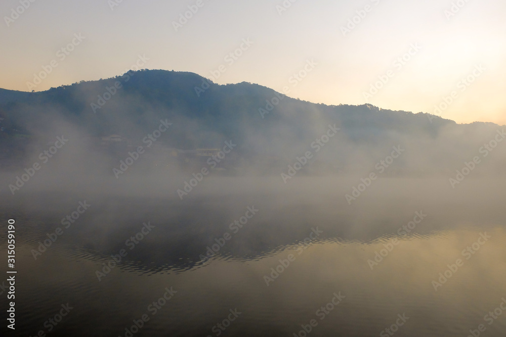 Mountain and forest over lake in the foggy day