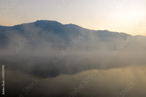 Mountain and forest over lake in the foggy day