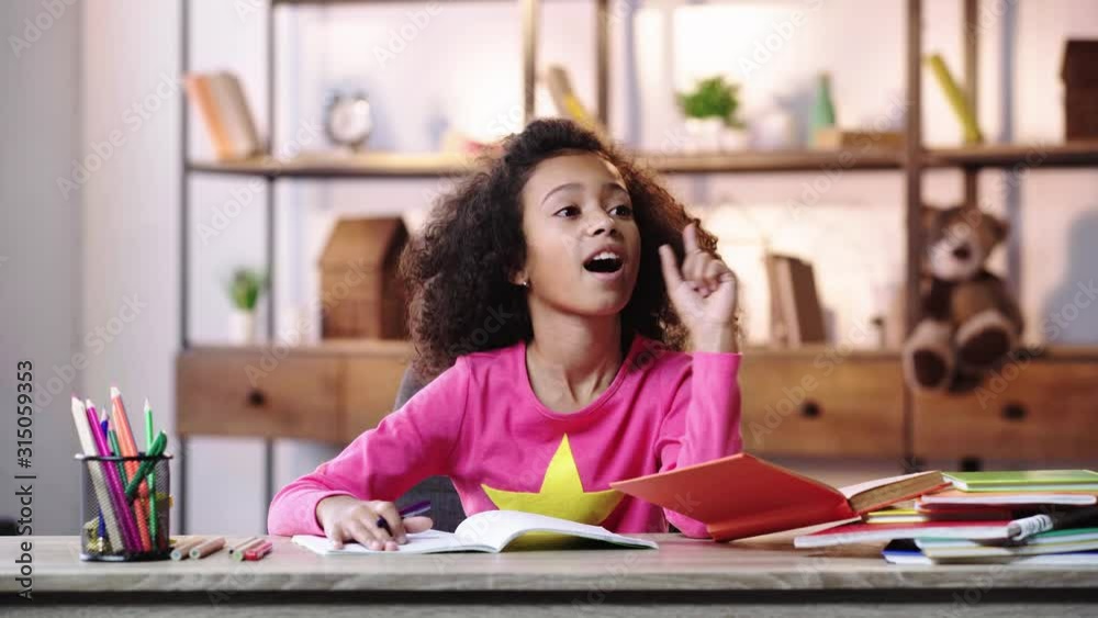 pensive african american child showing idea gesture and writing in copybook
